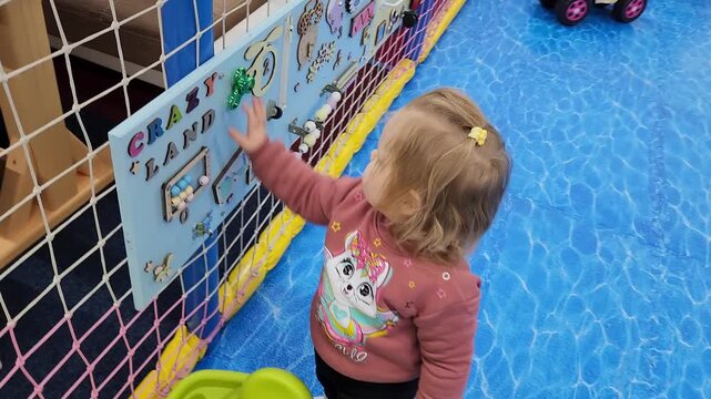 Cute toddler girl Sofia playing with interactive toys on a busy wall
