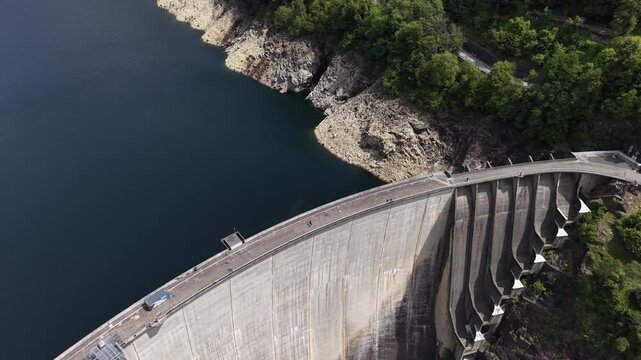 Aerial view of the massive Verzasca Dam arching over the valley with deep blue water and rocky cliffs in Gordola, Ticino, Switzerland.