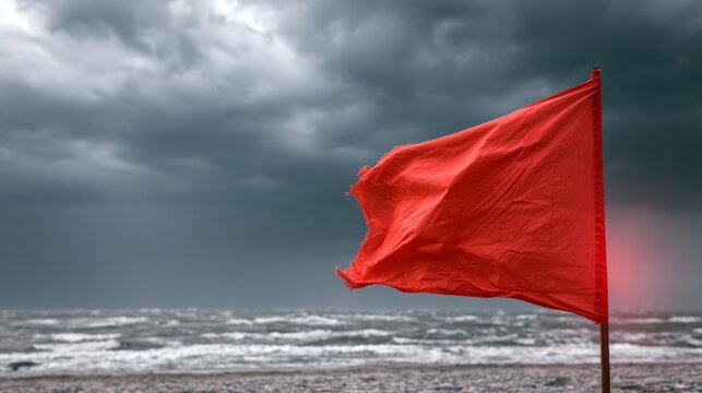Red warning flag on a wooden pole waving on a stormy beach with a turbulent sea and dramatic, dark clouds