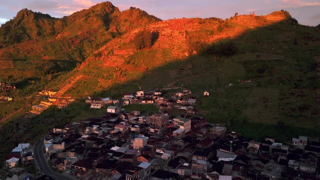 Aerial view of the Dieng plateau village with terraced agricultural fields on mountain slopes during golden hour sunset in Kejajar, Central Java, Indonesia.