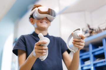 Innovative computer education for child with VR, Boy wearing virtual reality headset holding controllers in workshop © Parilov