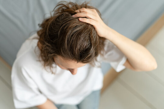 A woman carefully watches as first gray hairs emerge on her head. The mature adult observes gradual process of her hair changing color. Mother tracks progression of silver strands.