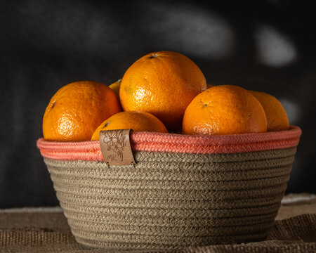 cesta nordica con cordon de algodon echa artesanal de color beige con borde tono salmon , con naranjas de estacion y fondo de luz de ventana 