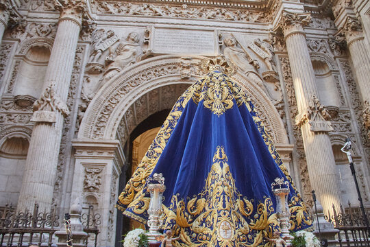Rear view of richly embroidered mantle on processional sculpture before cathedral entrance, highlighting Catholic symbolism, gold thread craftsmanship and ceremonial devotion