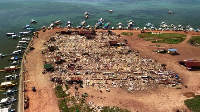 Aerial view of Coron coastal waste site in Palawan Philippines with docked outrigger boats shoreline debris makeshift structures water and dirt road