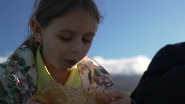 Child, Eating, Picnic food outdoors against bright blue sky during summer vacation.