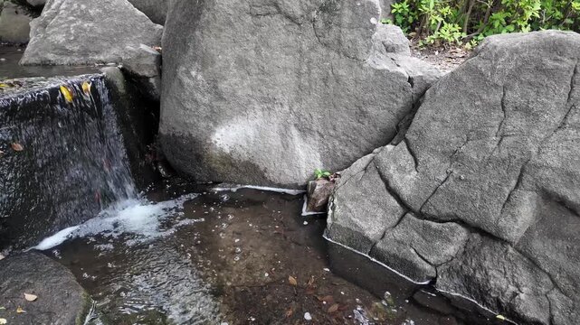 Close-up of clear water flowing down from large rocks, a babbling brook and a small waterfall in a park