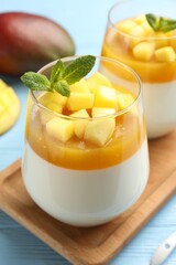 Fototapeta premium Delicious mango panna cotta with mint and fresh fruits on light blue wooden table, closeup
