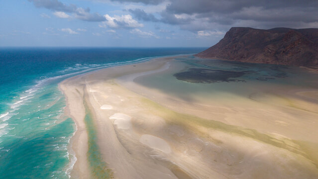 Aerial sandbar and turquoise lagoon by rocky coast