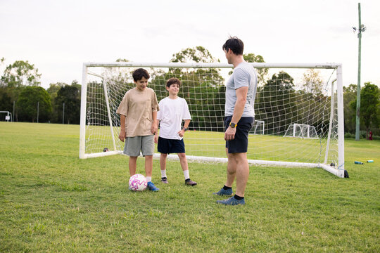 Adult man with two young boys in a huddle on grassy soccer field near goalpost