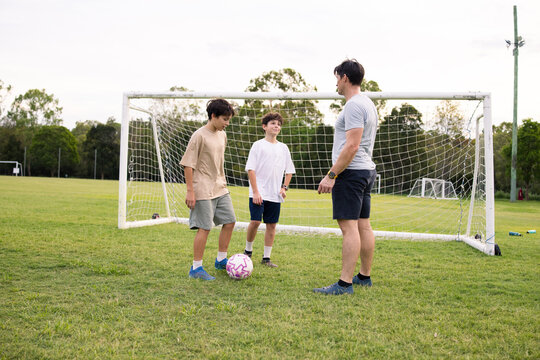 Adult man with two young boys in a huddle on grassy soccer field near goalpost