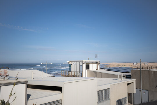 Modern coastal buildings with ocean waves and sandy dunes under a clear blue sky