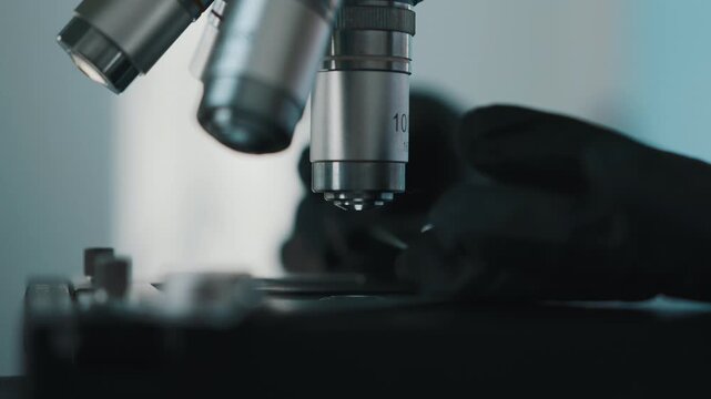 Laboratory technician placing glass slide under microscope for analysis