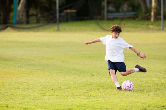 Young soccer player kicking soccer ball on grassy field