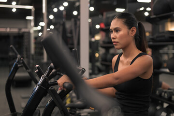 Fototapeta premium Determined Asian Woman Working Out on Air Bike at Gym at Night