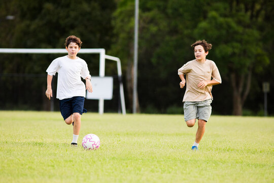 Two young soccer players running towards the soccer ball on grassy field