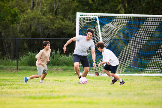 Father playing soccer with his sons on green soccer field