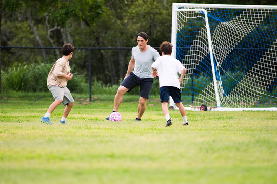 Father playing soccer with his sons on green soccer field