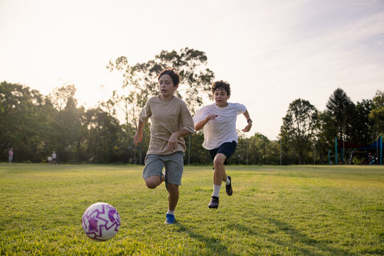 Two young boys playing soccer on a grassy field at sunset