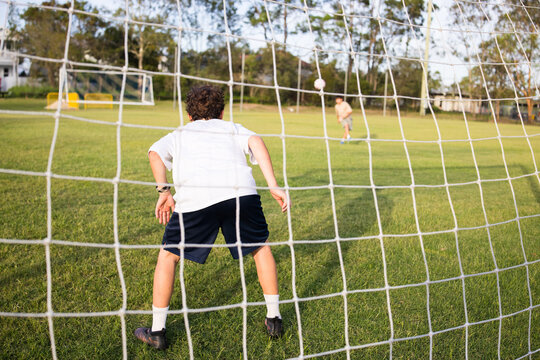 Young soccer player on defensive stance viewed through the soccer goal net during penalty kick