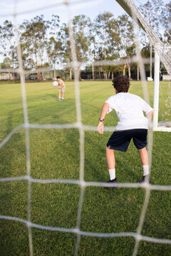 Young soccer player on defensive stance viewed through the soccer goal net during penalty kick