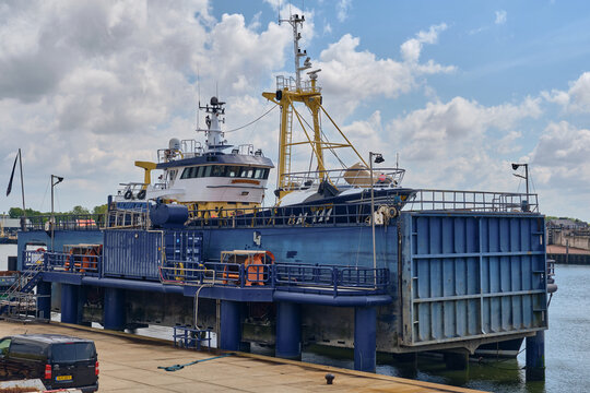 Den Oever, Netherlands - 18 May 2026: View of a British fleet vessel being renovated at a Dutch fishing repair wharf with industrial equipment under a cloudy sky.