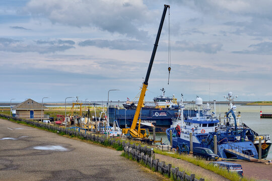 Den Oever, Netherlands - 18 May 2026: View of British fleet vessels being renovated at the Machinefabriek fishing repair wharf with a large yellow crane in the harbor.