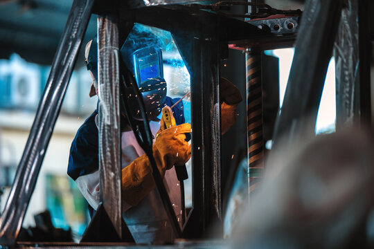 Industrial worker welding steel structure sparks protective mask leather gloves. Manual arc welding metal frame factory production line heavy industry metalwork fabrication process steel.