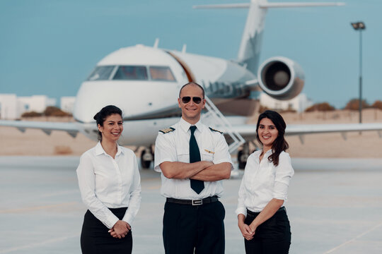 Pilot and two crew members posing in front of private jet on airport tarmac for business travel