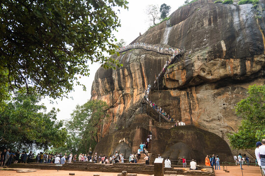 Sri Lanka - 21 February 2026: View of the Lion's Paw entrance at Sigiriya rock fortress with tourists climbing the steep metal staircase against the massive granite cliff.