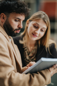 Two colleagues review a tablet while discussing documents and information. A focused business conversation between a man and a woman collaborating on work.