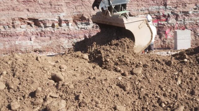 Digger attachment operating close-up, moving mounds of stony earth during infrastructure excavation and building site preparation work