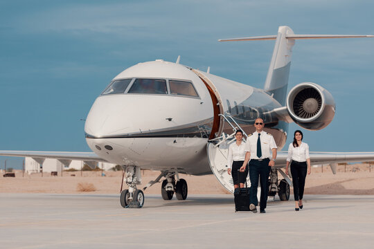 Business pilot and flight crew walking confidently from private jet on airport tarmac for corporate travel