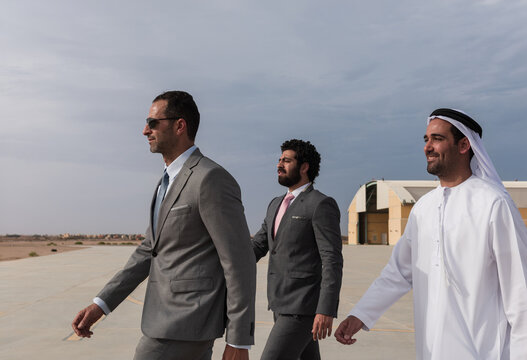 Businessmen and Emirati executive walking confidently on an airport tarmac beside hangars