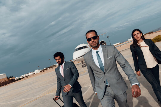 Business executives walking confidently from private jet on airport runway, corporate team travel and leadership