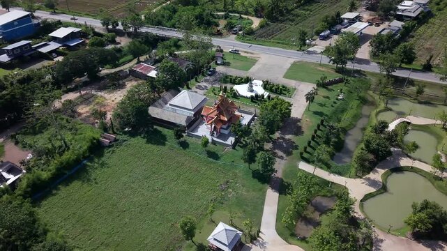 A high-angle aerial drone view revealing a serene temple complex with golden architecture, set beside a beautifully landscaped park featuring curved ponds, decorative bridges, and lush greenery, all s