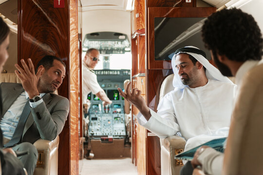 Business executives in conversation onboard a private jet with pilot visible in the cockpit