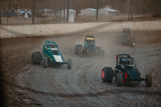 Sprint cars race on a dusty dirt track, kicking up clouds of dirt as they compete