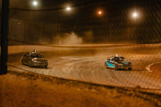 Dirt track racing at night with cars kicking up dust on the turn
