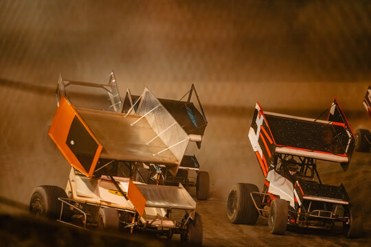 Sprint cars race on a dirt track, kicking up dust during competition