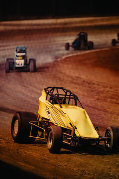 Yellow sprint car races on dirt track with other cars in the background