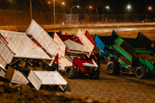 Sprint cars lined up on a dirt track at night preparing to race