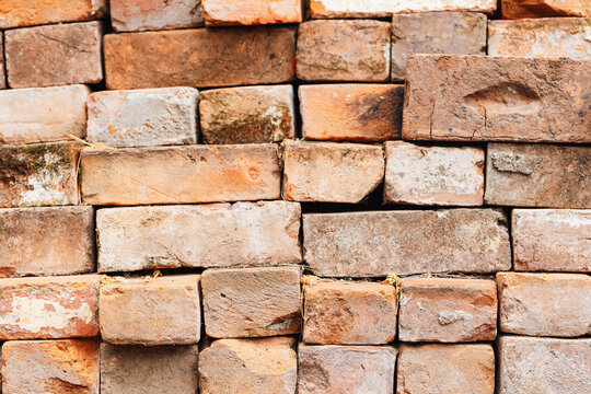 Close-up texture of a weathered stack of old, rustic red bricks with visible imperfections
