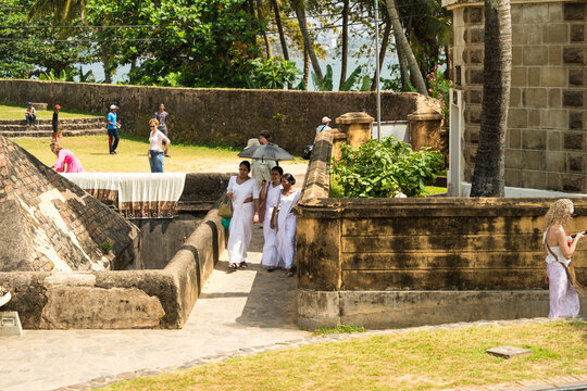 Galle, Sri Lanka - 04 February 2026: View of people walking along the historic stone ramparts of Galle Fort with palm trees and the ocean in the background.