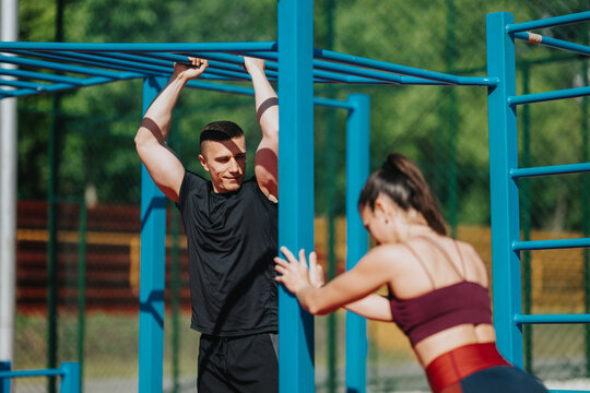 A young man and woman train on blue outdoor monkey bars performing strength exercises. The couple works out together in a sunny park fitness area.