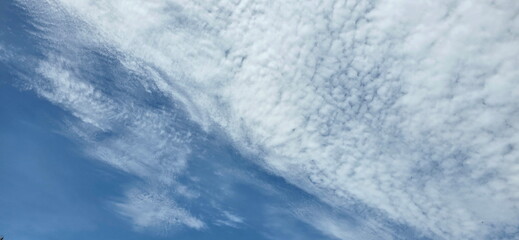 Backdrop is clear, light blue sky with sparse white clouds. Small white clouds,arranged in clusters resembling fish scales or ripples, create sky pattern often referred to as "ripple" or "cluster" sky © Vanchuree