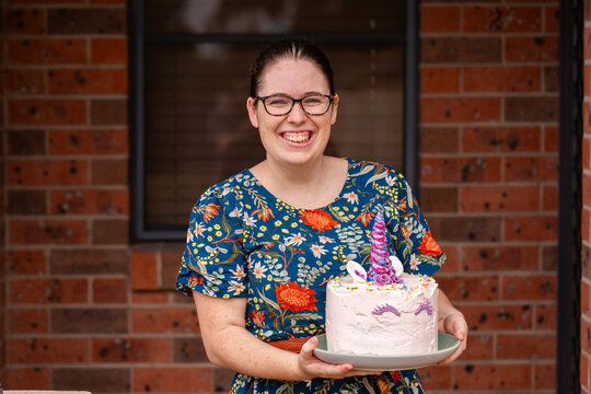 Smiling Aussie mum holding homemade childs unicorn birthday cake