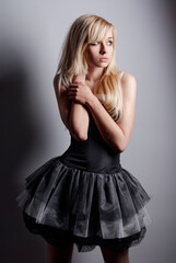 Fototapeta premium Blonde woman wearing a stylish black dress poses in a thoughtful manner against a studio backdrop, showcasing elegant fashion with a hint of mystery and introspection.