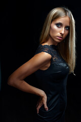Fototapeta premium Elegant blonde fashion model poses in a black lace dress against a dark background, conveying confidence, glamour and sophistication with dramatic studio lighting and a poised, intense expression.
