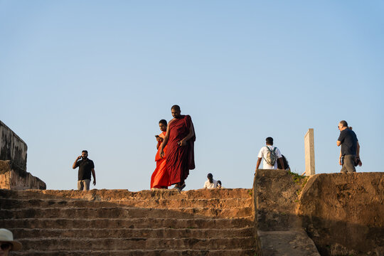Sri Lanka - 24 January 2026: View of Buddhist monks in traditional robes and tourists walking up ancient stone stairs against a clear blue sky.